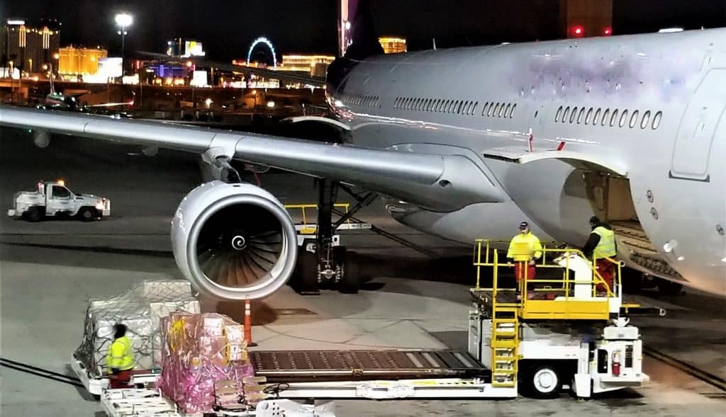 Cargo loading on an airplane at night with workers and equipment at the airport.