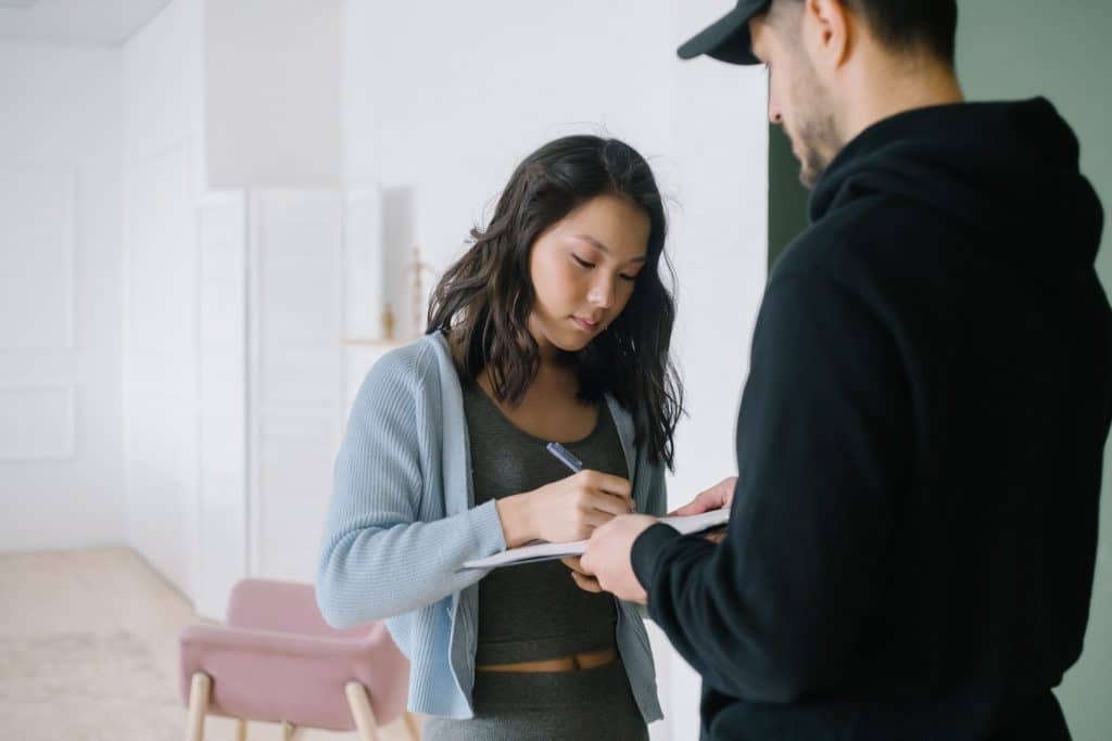 A woman in a light blue cardigan signing a document held by a man in a black hoodie, showcasing a professional interaction.