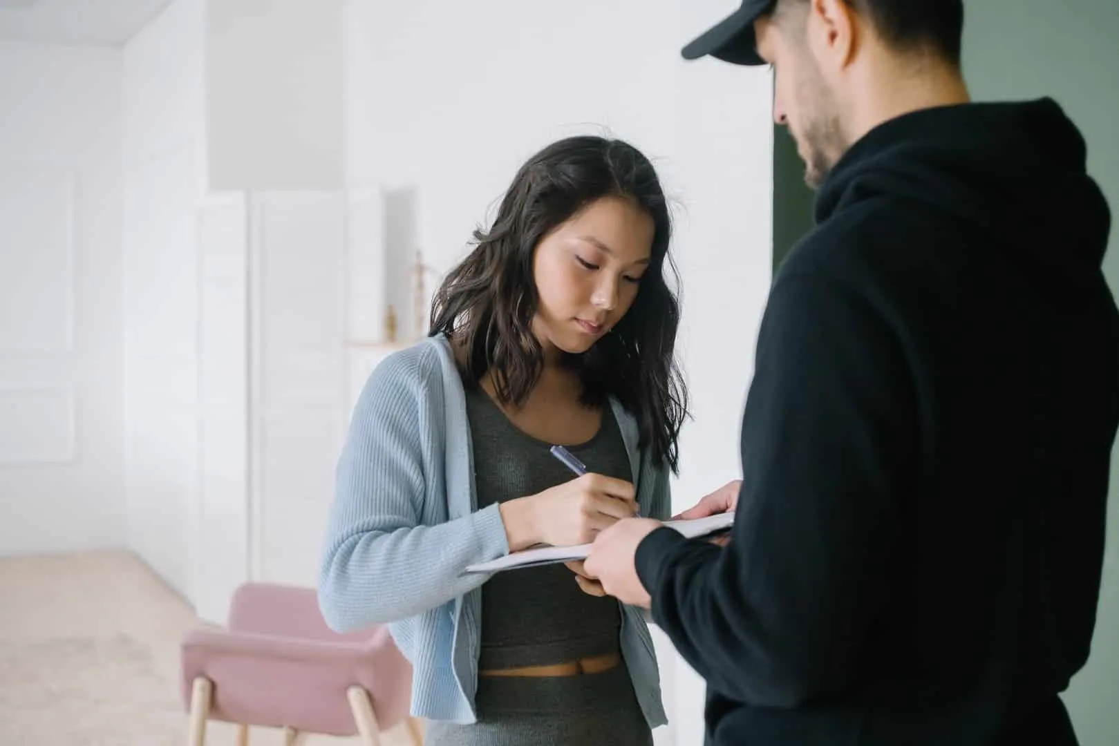 A woman in a light blue cardigan signing a document held by a man in a black hoodie, showcasing a professional interaction.